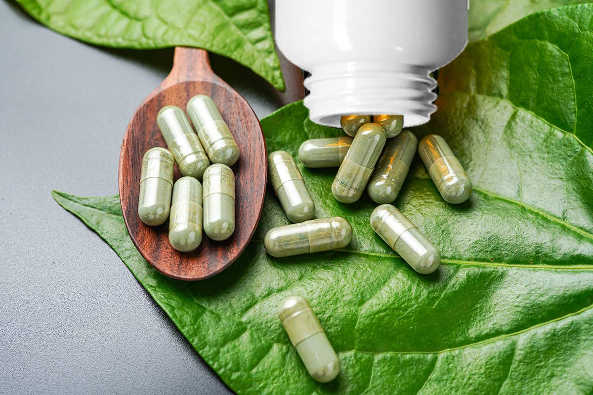 Airbiotic_una-pila-de-capsulas-de-hierbas-en-una-cuchara-de-madera-con-hierbas-y-hoja-de-pimienta-de-betel-verde-en-el-fondo